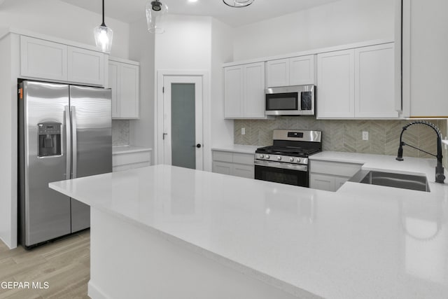kitchen with appliances with stainless steel finishes, a sink, tasteful backsplash, and light wood-style floors