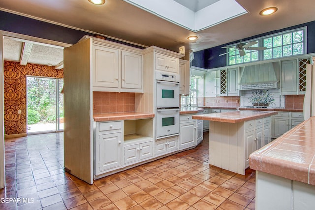 6041 Torrey Pines Dr, El Paso, TX 79912 - kitchen with tasteful backsplash, white double oven, plenty of natural light, tile countertops, and premium range hood