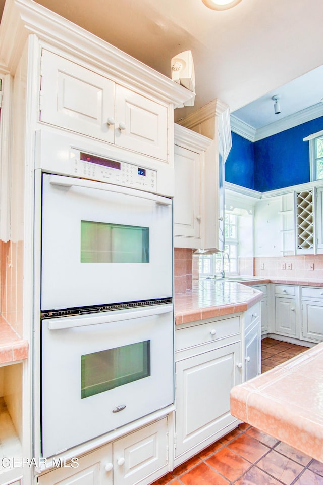 6041 Torrey Pines Dr, El Paso, TX 79912 - kitchen featuring white cabinetry, decorative backsplash, white double oven, a sink, and tile countertops
