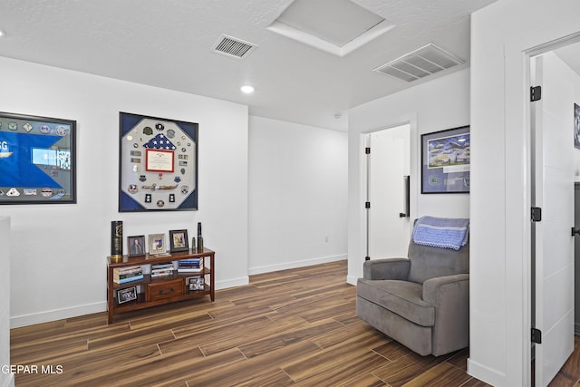 sitting room with dark wood-type flooring, visible vents, and baseboards