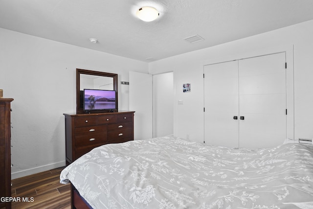 bedroom with dark wood finished floors, baseboards, visible vents, and a closet