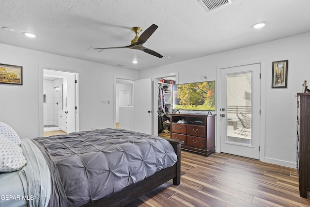bedroom with visible vents, access to exterior, wood finished floors, ensuite bath, and a walk in closet