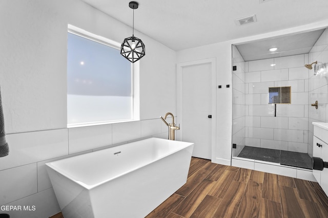 full bath with a stall shower, visible vents, wood finished floors, and a soaking tub