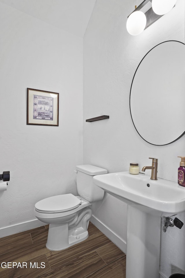 half bath featuring a sink, wood finished floors, toilet, and baseboards