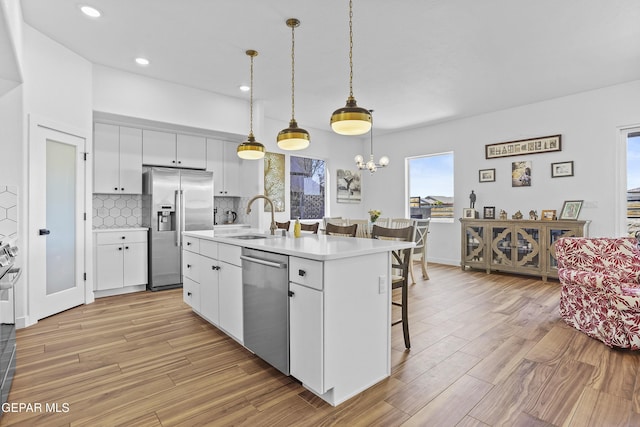 kitchen with appliances with stainless steel finishes, light countertops, white cabinets, a kitchen bar, and a sink