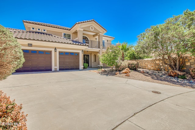 mediterranean / spanish home featuring driveway, a tile roof, a balcony, an attached garage, and stucco siding