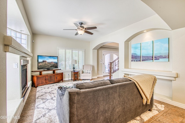 living room with tile patterned flooring, arched walkways, a glass covered fireplace, a ceiling fan, and baseboards