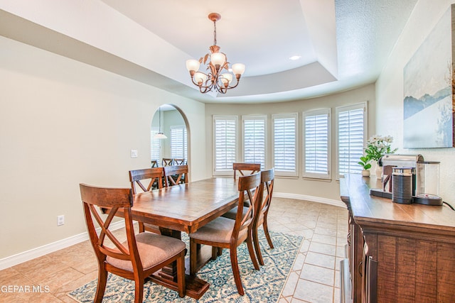 dining room with an inviting chandelier, a raised ceiling, arched walkways, baseboards, and light tile patterned floors