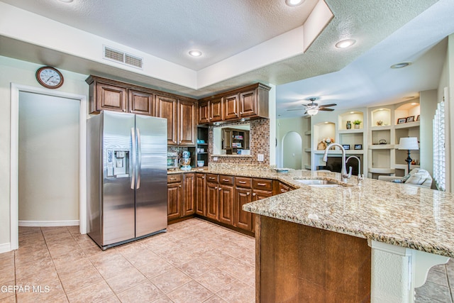 kitchen featuring light stone counters, a sink, stainless steel fridge with ice dispenser, a textured ceiling, and visible vents