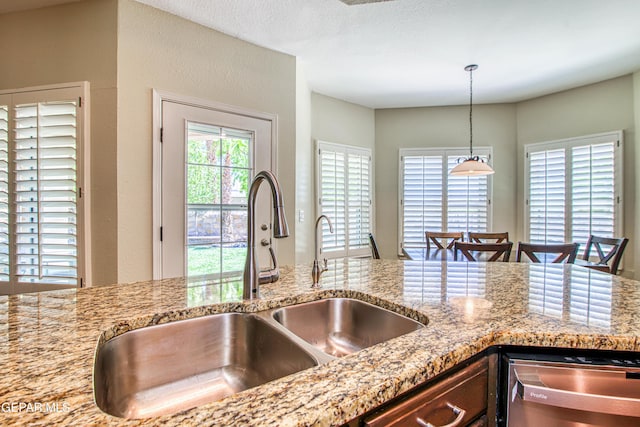 kitchen with stainless steel dishwasher, a sink, decorative light fixtures, and light stone countertops