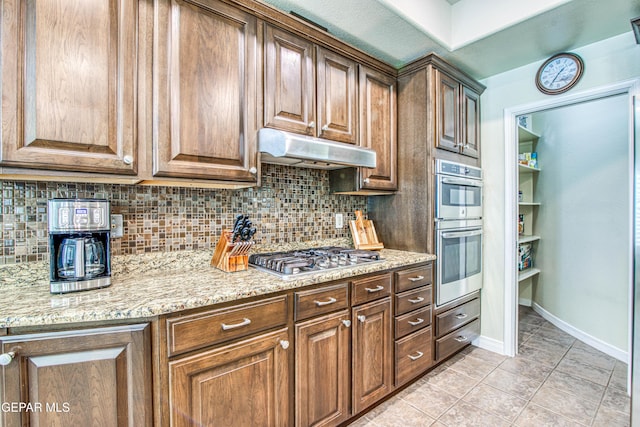 kitchen featuring appliances with stainless steel finishes, backsplash, under cabinet range hood, and light stone counters
