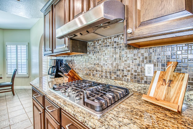 kitchen with backsplash, stainless steel gas cooktop, baseboards, under cabinet range hood, and light tile patterned flooring