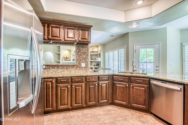 kitchen featuring appliances with stainless steel finishes, dark brown cabinets, a sink, light stone counters, and light tile patterned flooring