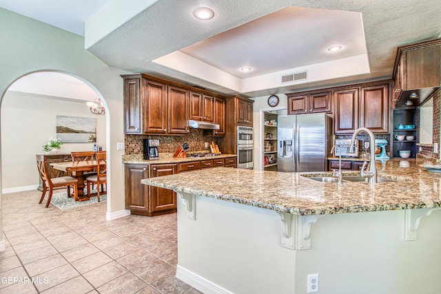 kitchen with light stone countertops, appliances with stainless steel finishes, a sink, a kitchen breakfast bar, and visible vents
