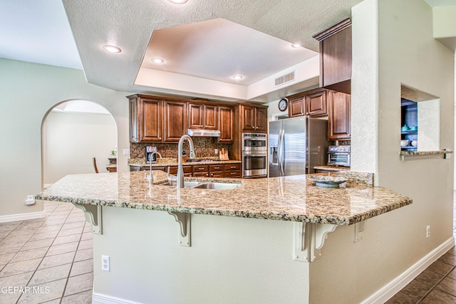 kitchen featuring visible vents, a sink, baseboards, a breakfast bar, and stainless steel appliances
