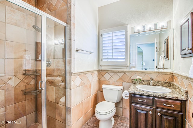 bathroom featuring wainscoting, vanity, toilet, tile walls, and a stall shower