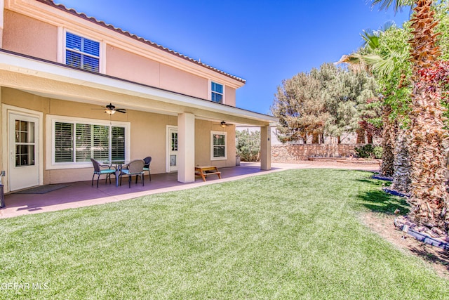 back of property with a lawn, ceiling fan, and stucco siding