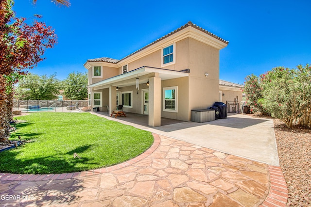 rear view of house with fence, a tile roof, ceiling fan, stucco siding, and a yard