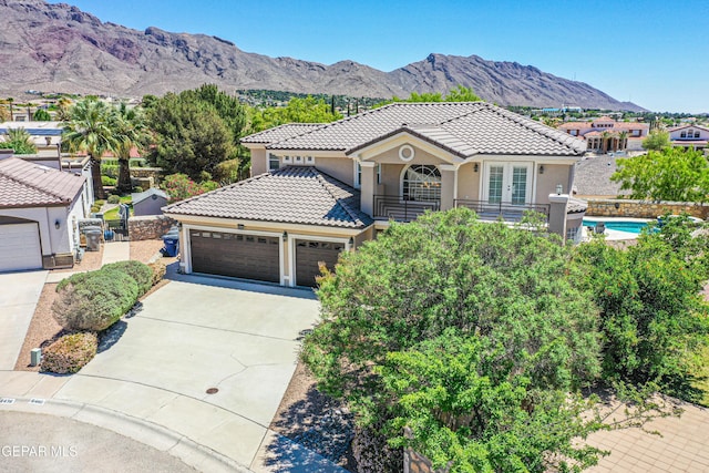 mediterranean / spanish-style house with french doors, a tile roof, a mountain view, concrete driveway, and stucco siding
