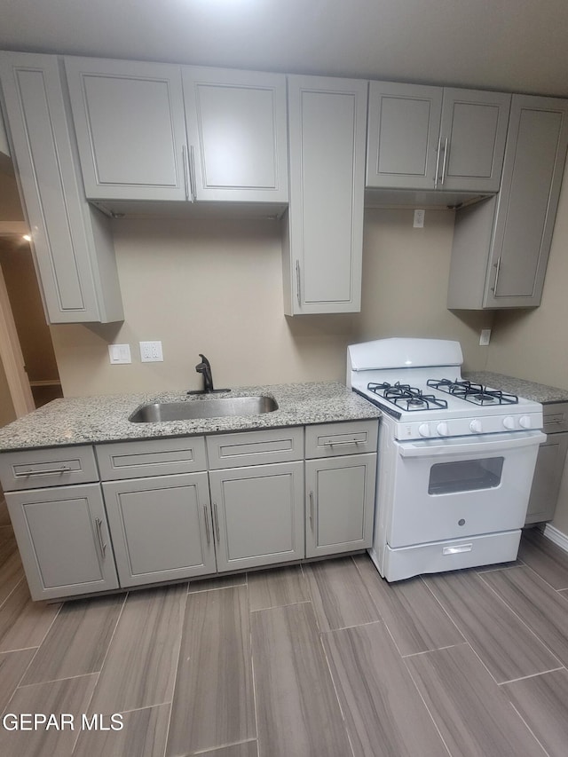 11531 Ernest Rd, Socorro, TX 79927 - kitchen featuring white range with gas stovetop, a sink, gray cabinets, wood finish floors, and light stone countertops