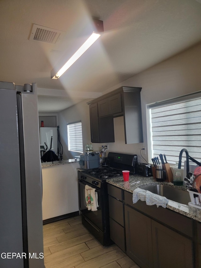 11531 Ernest Rd, Socorro, TX 79927 - kitchen with black range with gas stovetop, freestanding refrigerator, a sink, light wood finished floors, and light stone counters