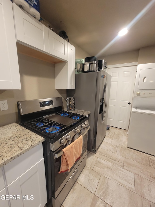 11531 Ernest Rd, Socorro, TX 79927 - kitchen with stainless steel range with gas stovetop, estacked washer and dryer, white cabinets, light marble finish floors, and light stone countertops