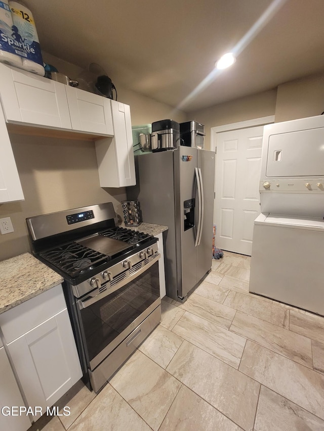 11531 Ernest Rd, Socorro, TX 79927 - kitchen with appliances with stainless steel finishes, stacked washer and clothes dryer, white cabinetry, and light stone countertops