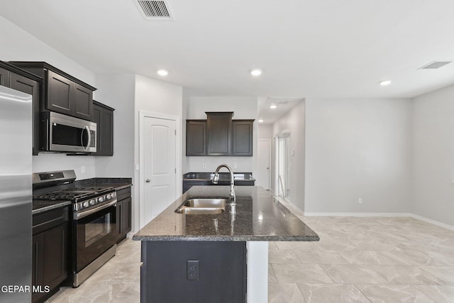 kitchen with appliances with stainless steel finishes, a sink, dark stone countertops, visible vents, and a center island with sink