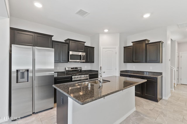 kitchen with visible vents, a center island with sink, a sink, dark stone counters, and stainless steel appliances