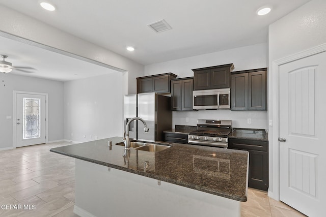 kitchen featuring visible vents, a sink, dark stone countertops, stainless steel appliances, and an island with sink