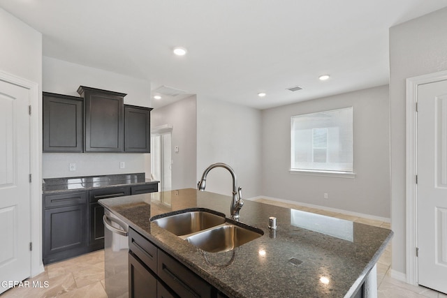 kitchen featuring dark stone counters, a center island with sink, a sink, and dishwasher