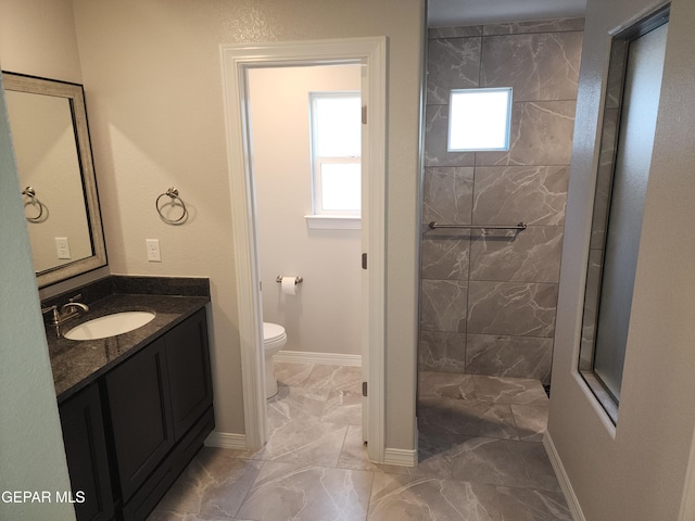 full bath featuring a tile shower, vanity, toilet, marble finish floor, and baseboards