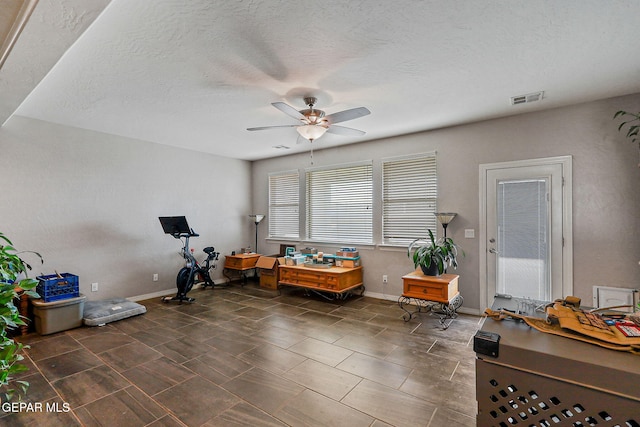 interior space with baseboards, a ceiling fan, a textured ceiling, and visible vents