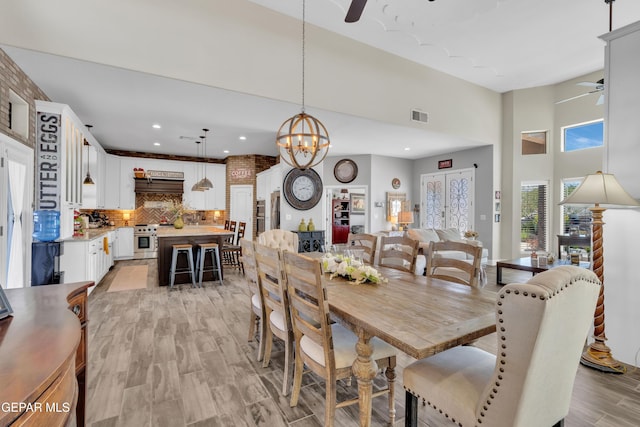 dining room featuring visible vents, light wood-style floors, recessed lighting, a towering ceiling, and ceiling fan with notable chandelier