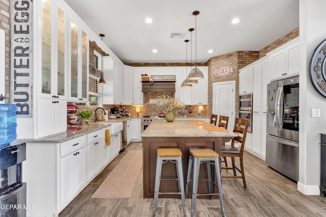 kitchen with a sink, stainless steel appliances, visible vents, white cabinetry, and a kitchen island