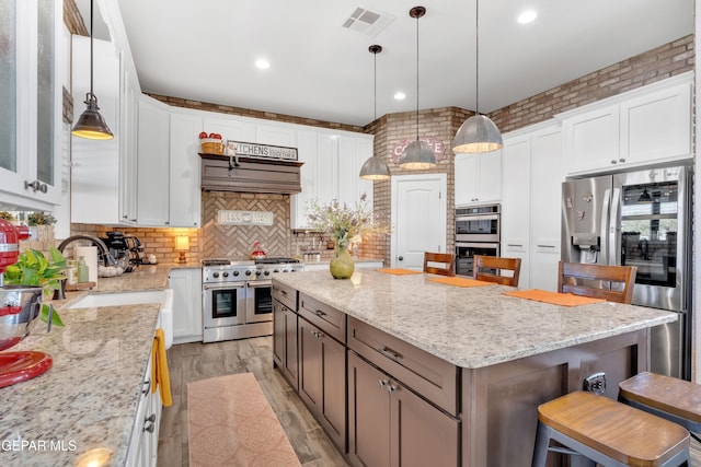 kitchen featuring stainless steel appliances, a kitchen island, a kitchen bar, white cabinetry, and visible vents