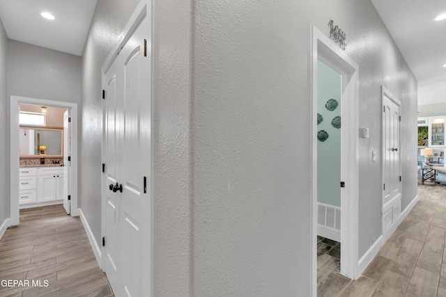 hallway featuring wood tiled floor, a textured wall, recessed lighting, and baseboards