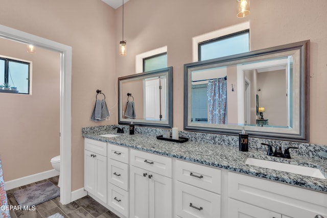 bathroom featuring toilet, double vanity, a sink, and baseboards