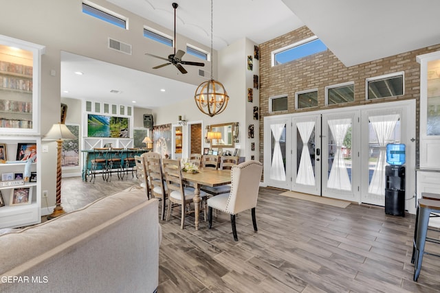 dining area featuring visible vents, wood finished floors, ceiling fan with notable chandelier, and a towering ceiling