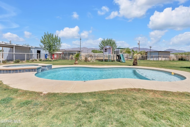 view of swimming pool with a pool with connected hot tub, fence, a playground, and a lawn