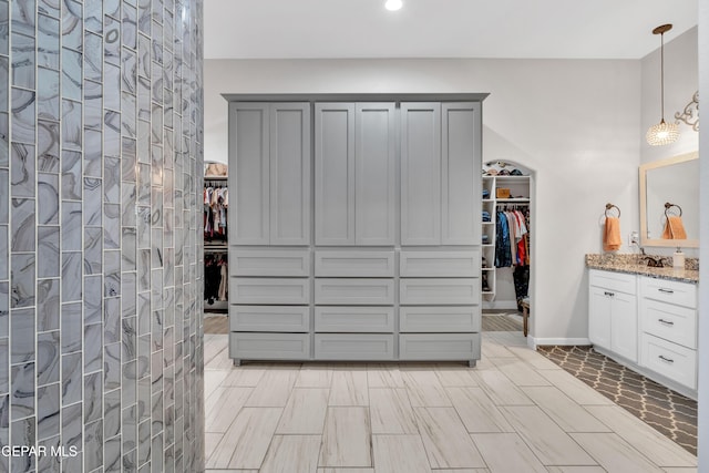bathroom featuring a tile shower, recessed lighting, a walk in closet, and vanity