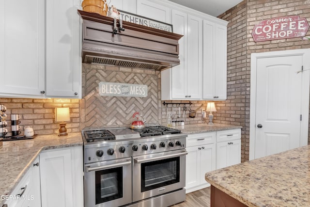 kitchen with custom exhaust hood, backsplash, white cabinets, and range with two ovens