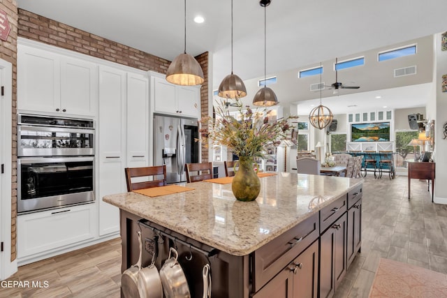 kitchen with light stone countertops, appliances with stainless steel finishes, white cabinets, visible vents, and a ceiling fan