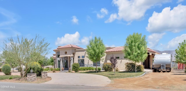 mediterranean / spanish-style house featuring curved driveway, stucco siding, and a tiled roof