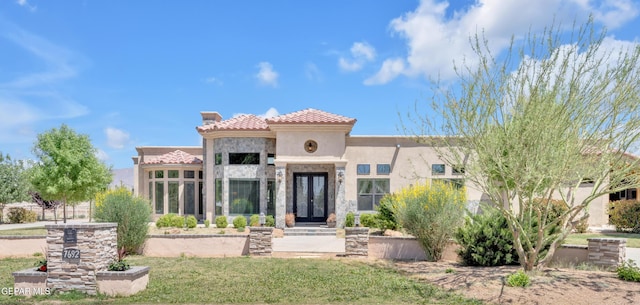 view of front facade with a tile roof, stone siding, a chimney, stucco siding, and french doors