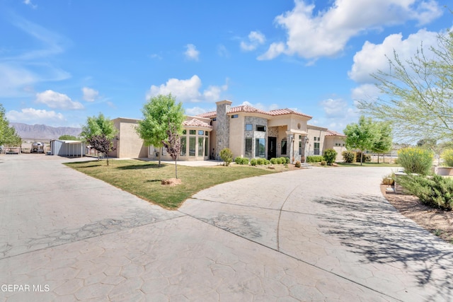 view of front facade featuring a tile roof, a mountain view, curved driveway, stucco siding, and a front lawn