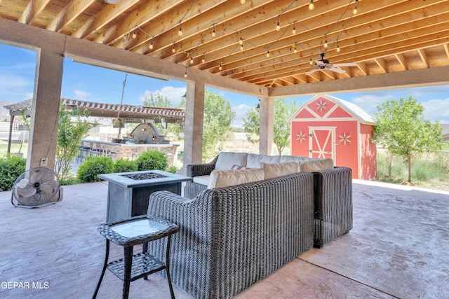 view of patio / terrace featuring a storage unit, ceiling fan, an outdoor living space with a fire pit, and an outbuilding