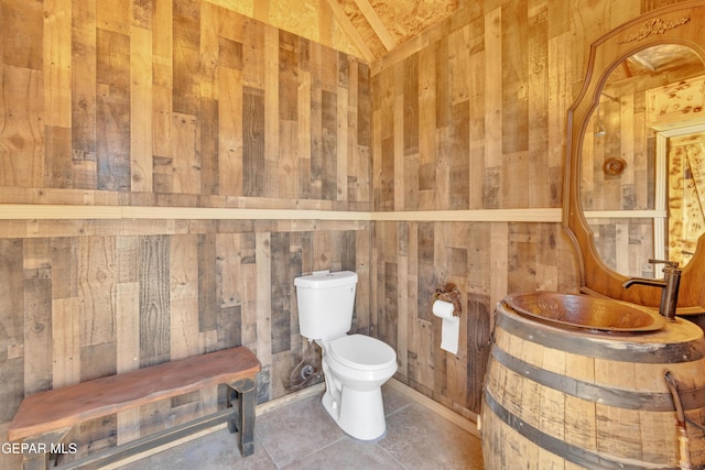 half bath featuring wood walls, toilet, and vaulted ceiling
