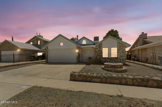 view of front of home with fence, an attached garage, concrete driveway, and stone siding