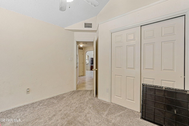 unfurnished bedroom featuring light colored carpet, arched walkways, lofted ceiling, visible vents, and a closet